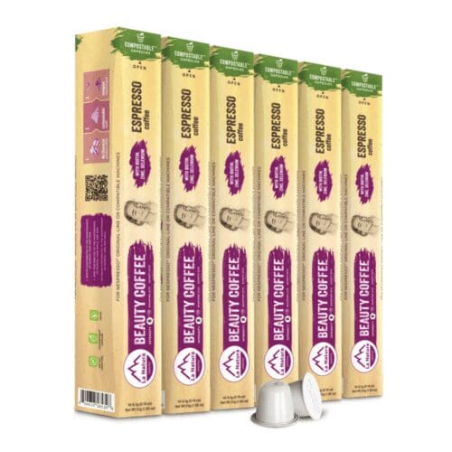 A row of five boxes of "Beauty Coffee" compostable espresso capsules is displayed upright. The beige packaging, accented in green and purple, showcases images of coffee beans, coffee cups, and portraits. Two white capsules are placed in front, embodying the beauty of sustainable brewing.
