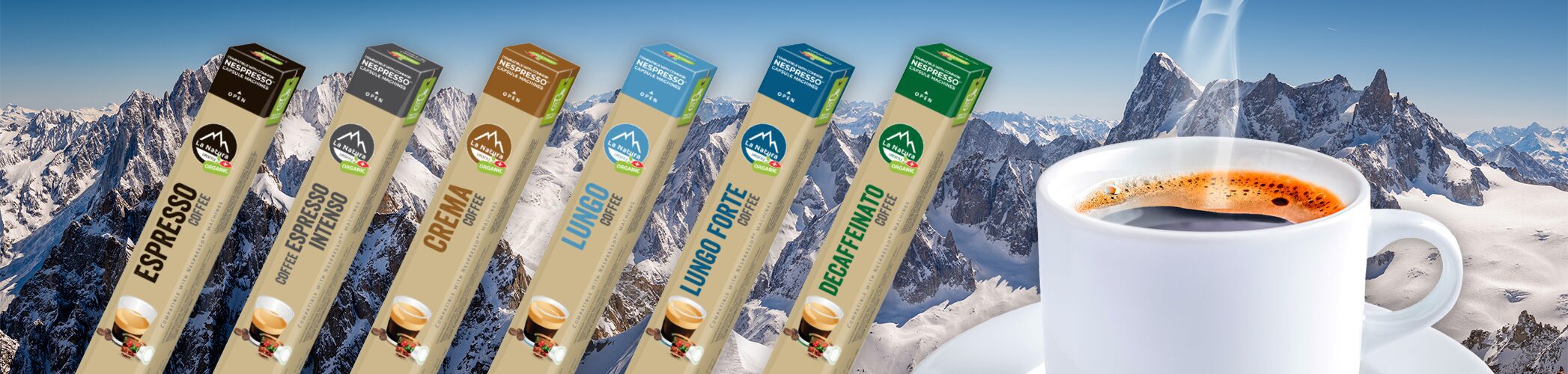 A steaming cup of La Natura coffee with a snowy mountain range in the background. In the foreground are six colorful coffee pod packages labeled (left to right): Espresso, Intenso, Crema, Lungo, Lungo Forte, and Decaffeinato. Celebrate Swiss Coffee Month with every sip!